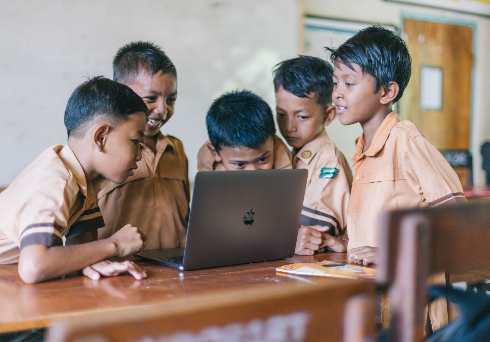 A group of children are looking at a laptop computer in a classroom.
