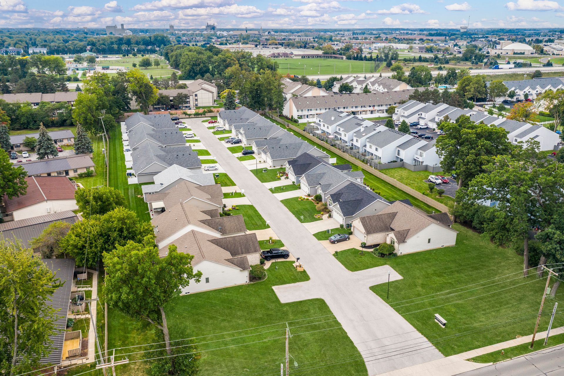 Aerial view of townhouses in a suburban neighborhood with green lawns and a paved road.