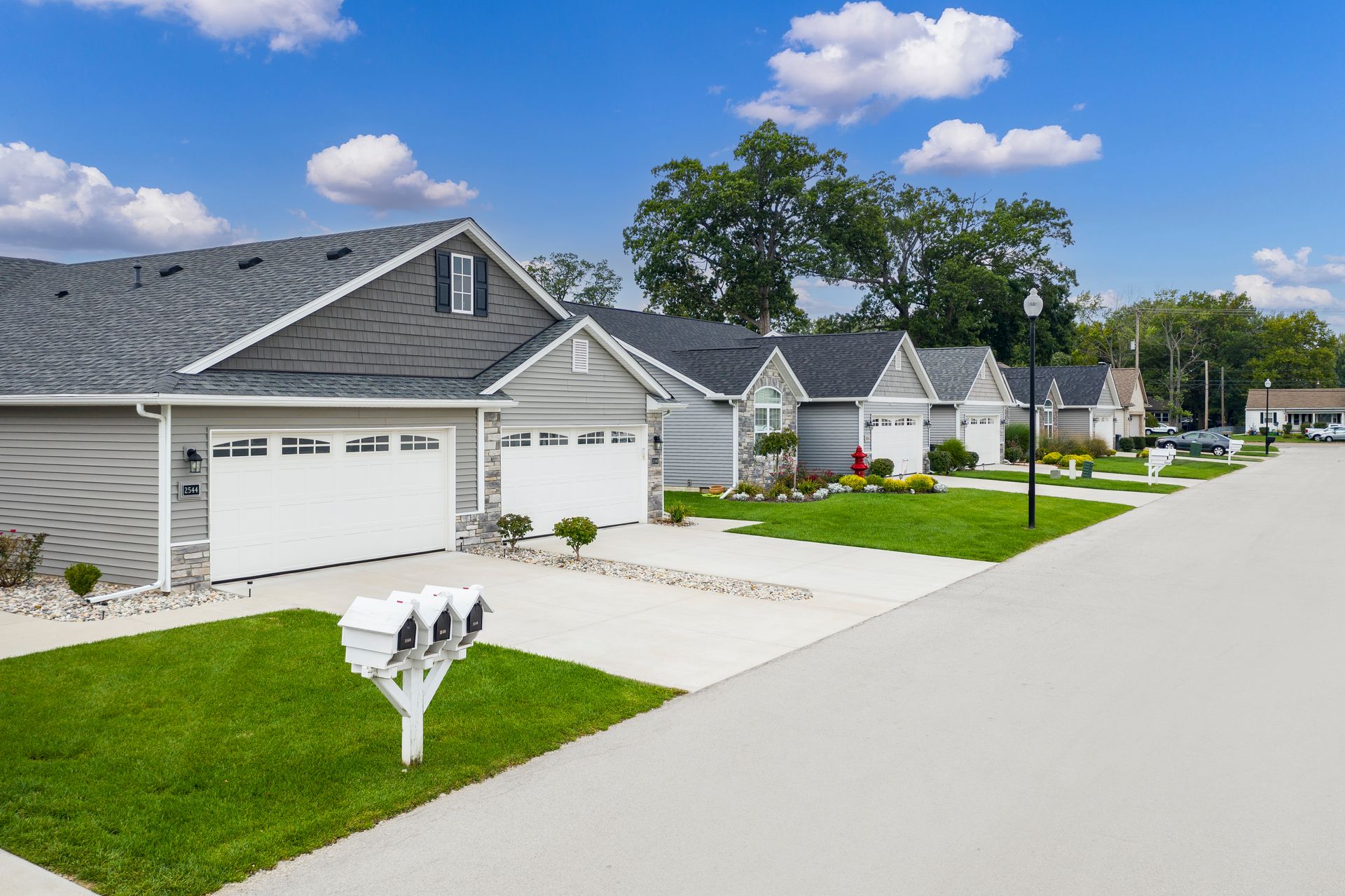 Row of houses with attached garages and driveways, on a sunny street, green lawns.