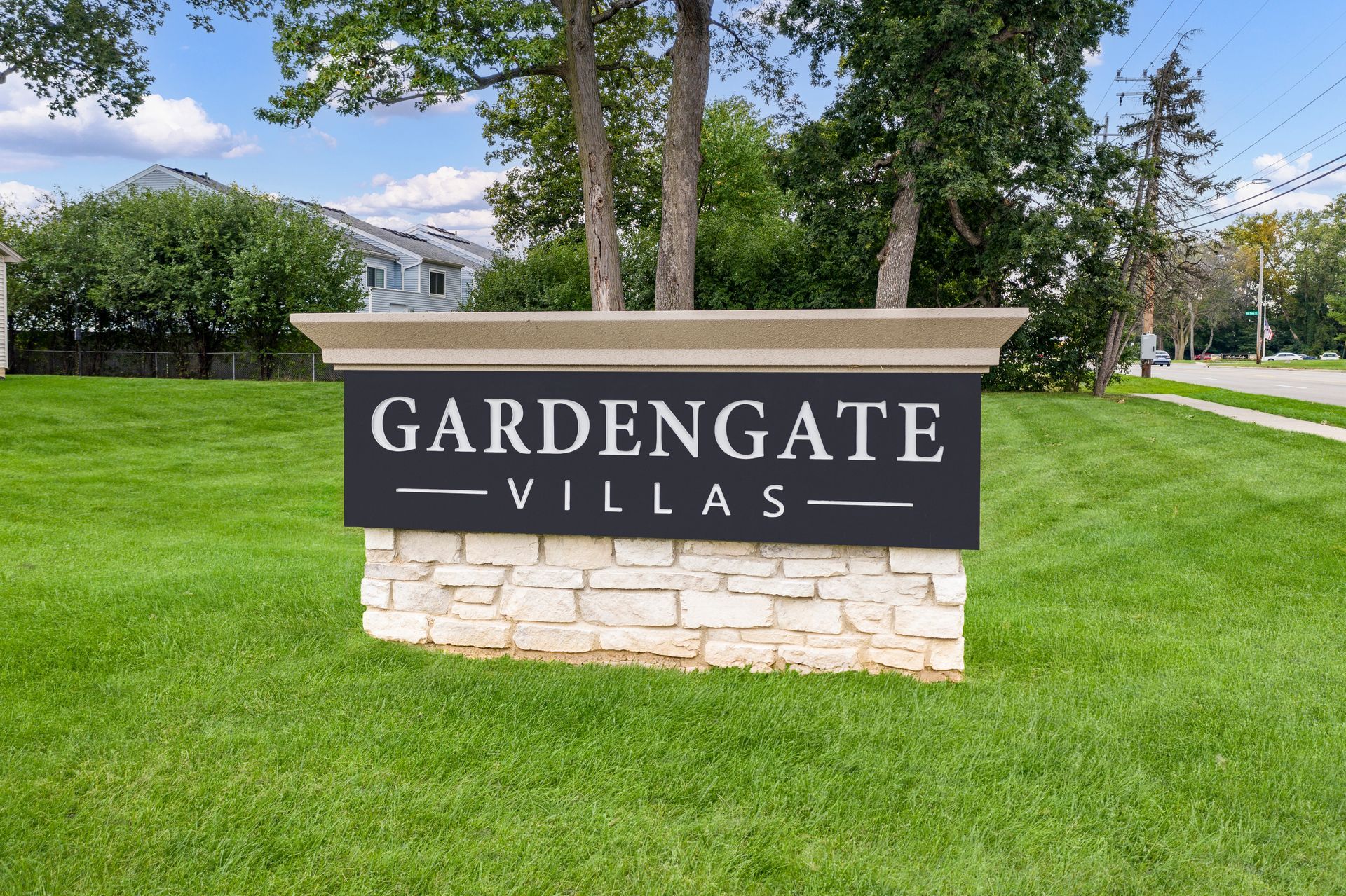 Gardengate Villas sign with black text on a dark backdrop, set on a stone base, green lawn.