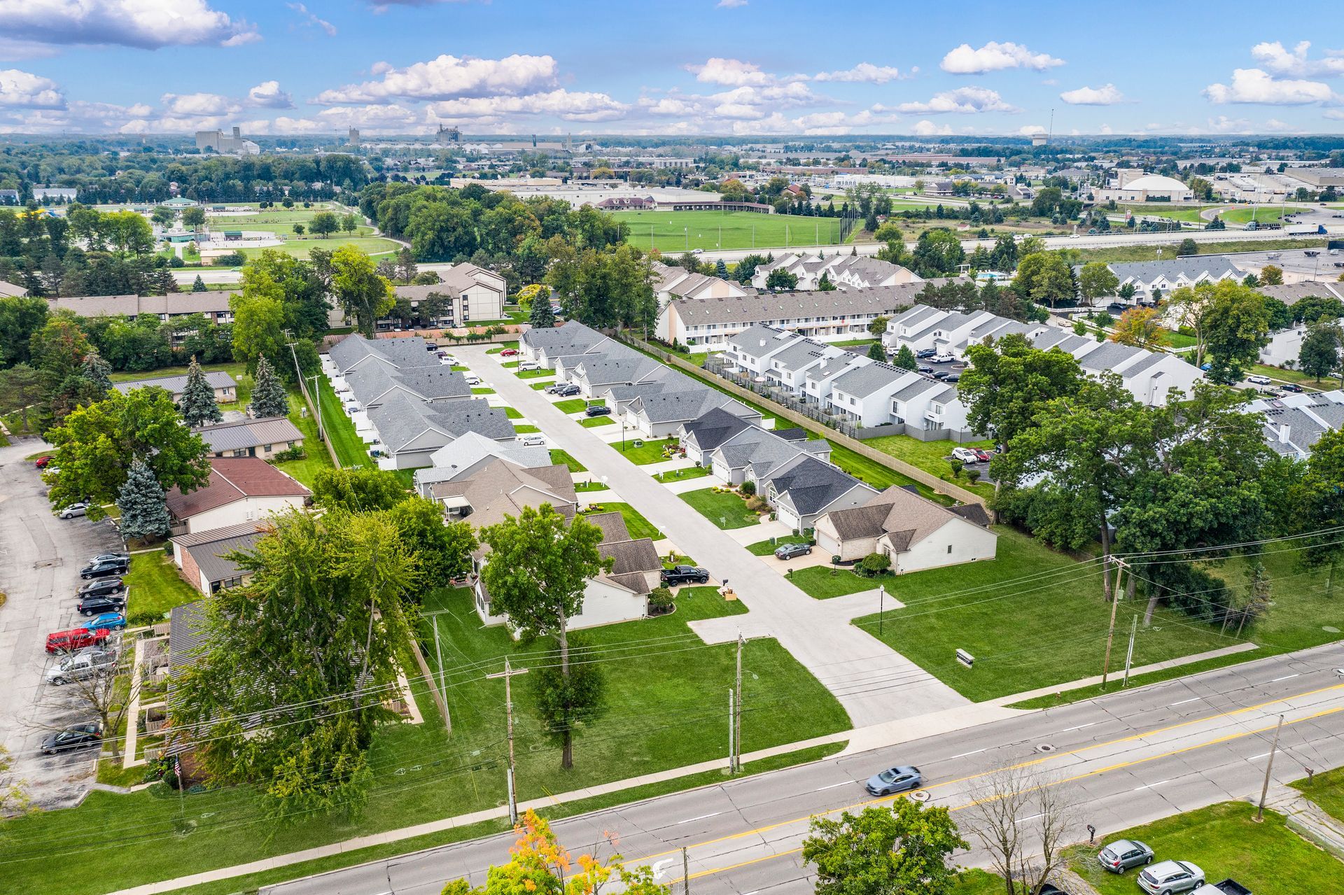 Aerial view of a suburban neighborhood with rows of houses, green lawns, and a road.