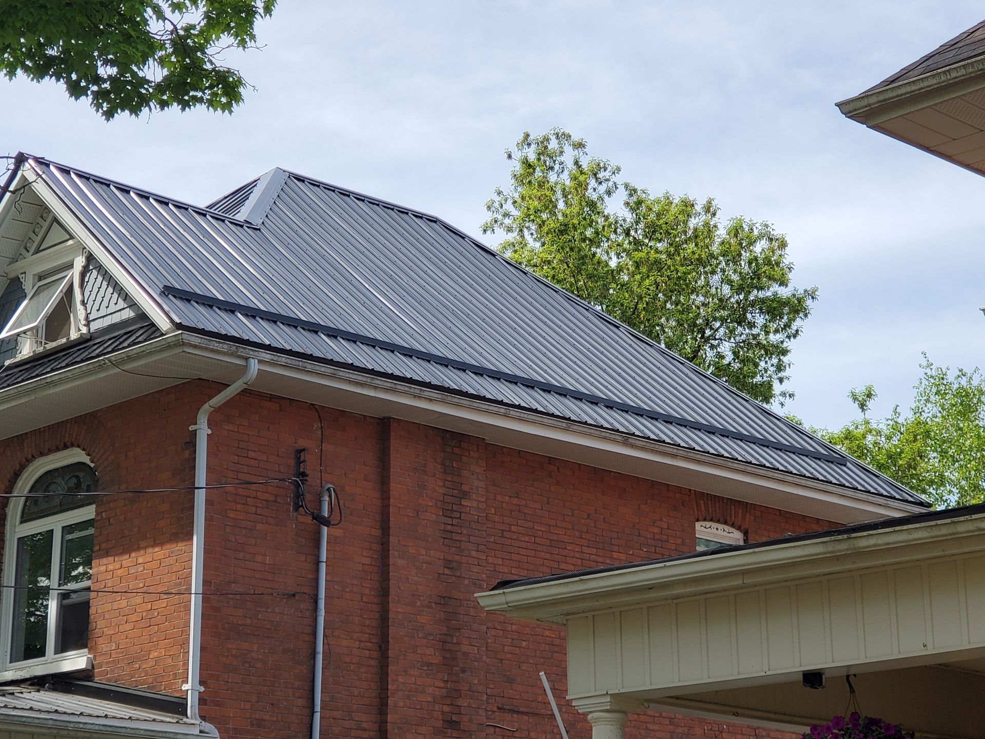 A brick house with a black roof and a white porch.