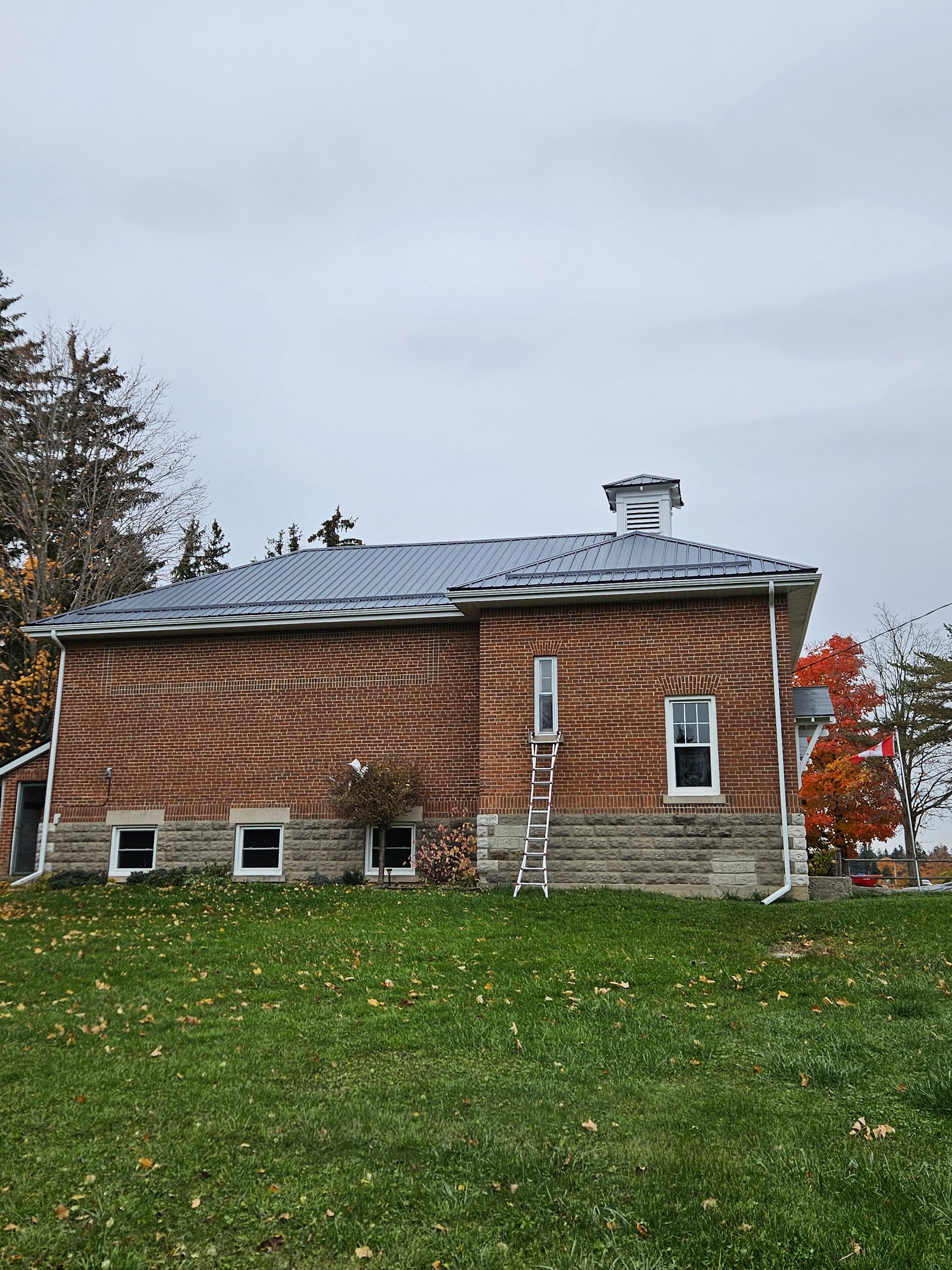 A brick building with a metal roof is sitting on top of a grassy hill.