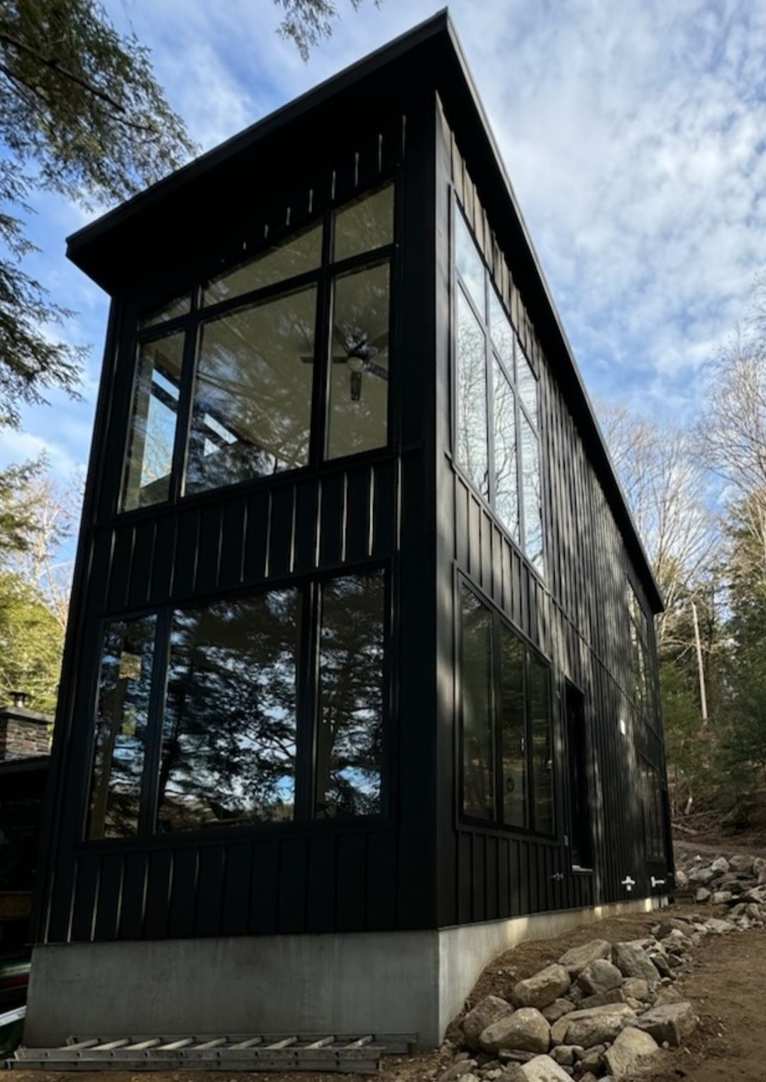 A black house with a lot of windows is surrounded by trees.