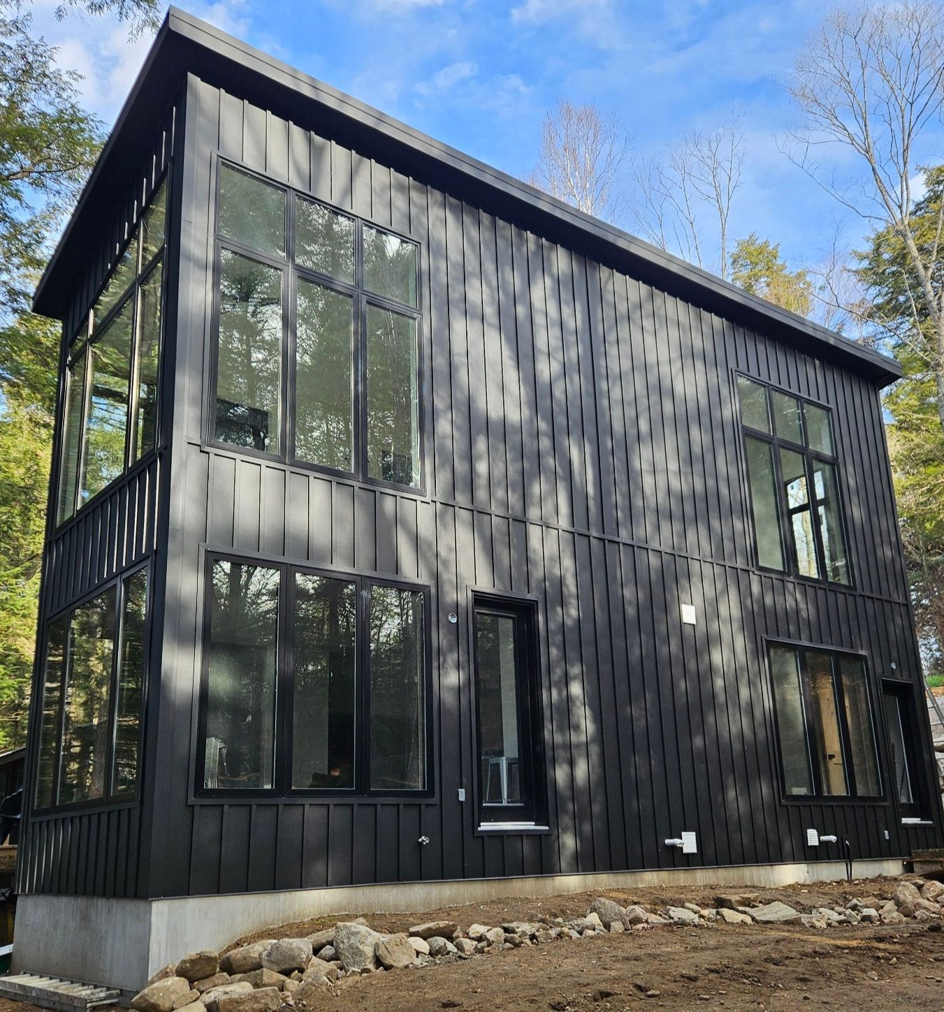 A black house with a lot of windows is surrounded by trees.