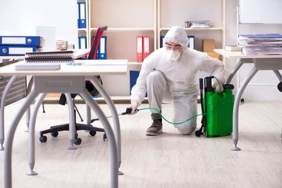 Un uomo con una tuta protettiva sta disinfettando un ufficio.