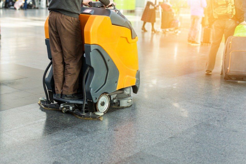 Un uomo sta pulendo il pavimento di un aeroporto con una macchina.
