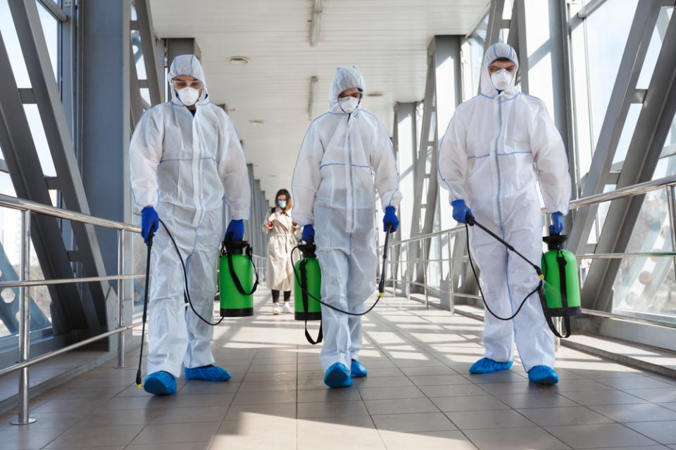 Un gruppo di persone con tute protettive e maschere sta disinfettando un edificio.