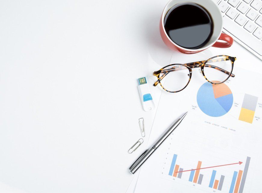 A cup of coffee , glasses , a pen , and a graph on a table.