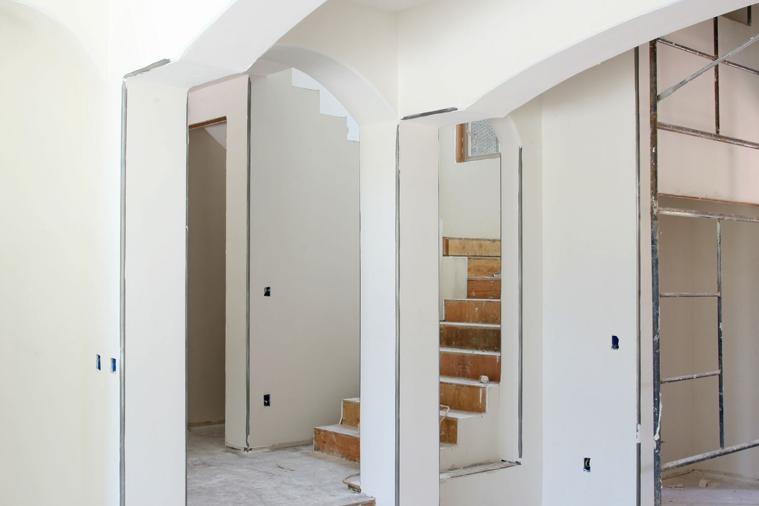 There is a staircase in the middle of the room with just finished drywall. 