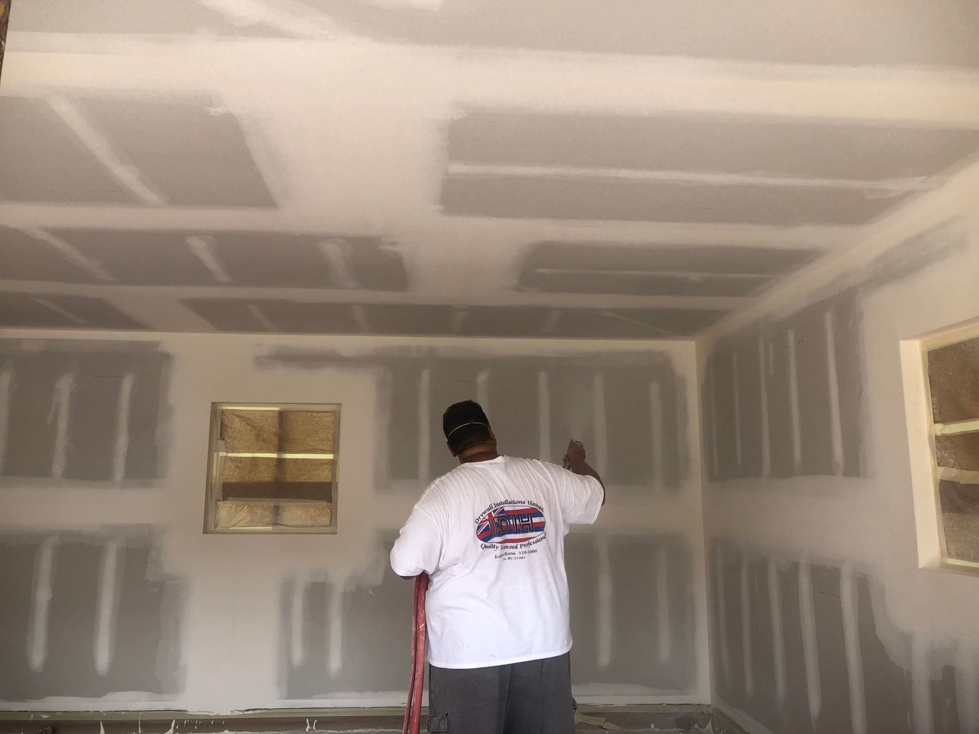 A man in a white shirt is drywalling the ceiling of a room