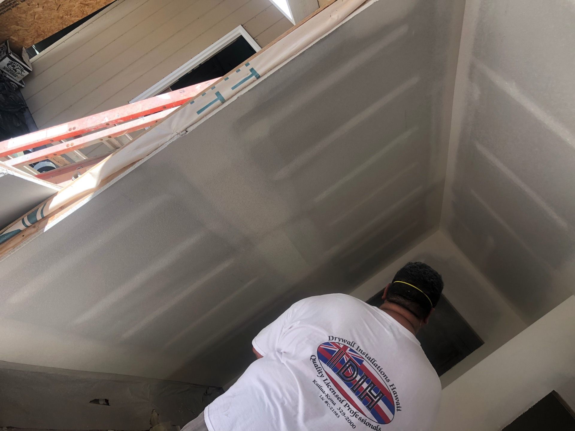 A man in a white shirt is standing in a room with a ladder.