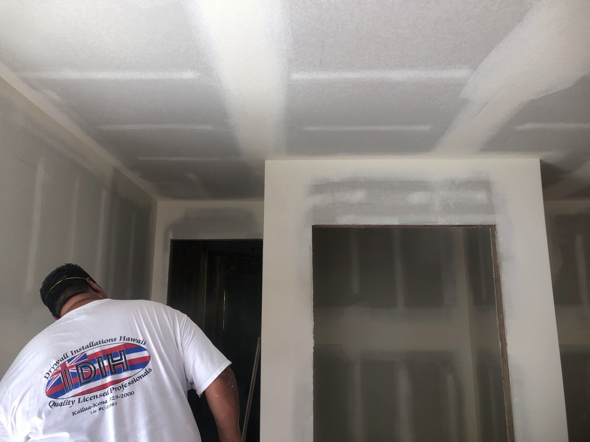 A man in a white shirt is working on a ceiling in a room.