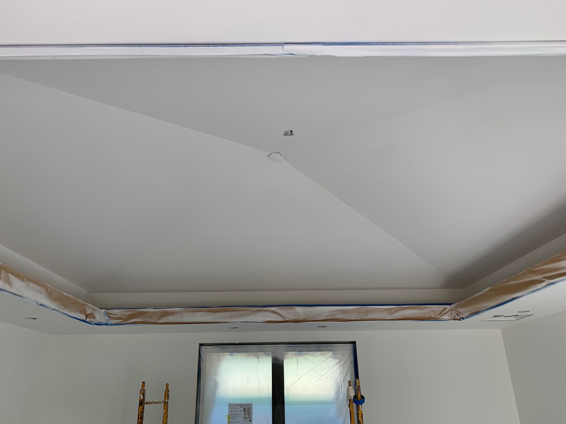 A ceiling is being painted in a room with a window.