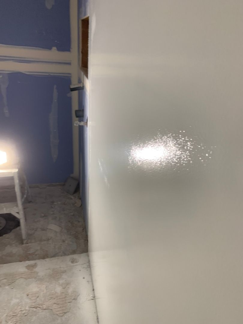 A white wall is being painted in a room with blue walls.