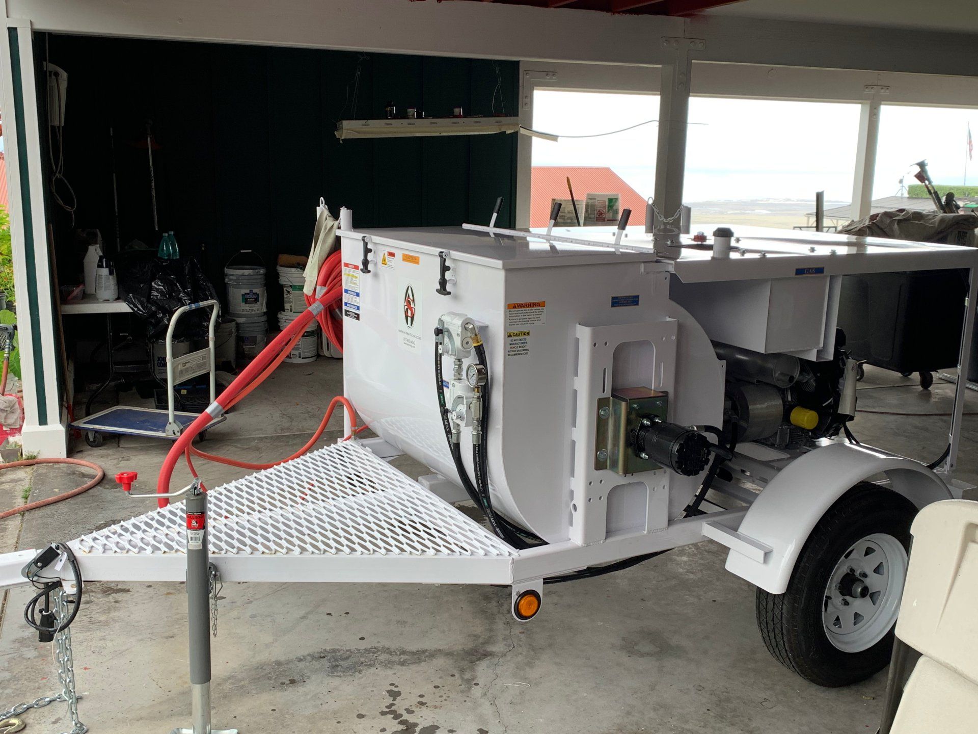 A white trailer with a hose attached to it is parked in a garage.