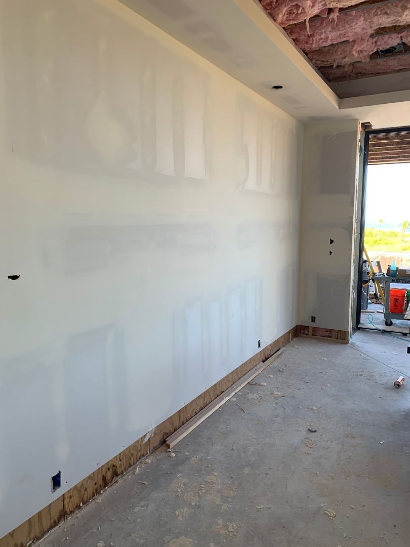 An empty room with a white wall and a concrete floor with finished drywall.