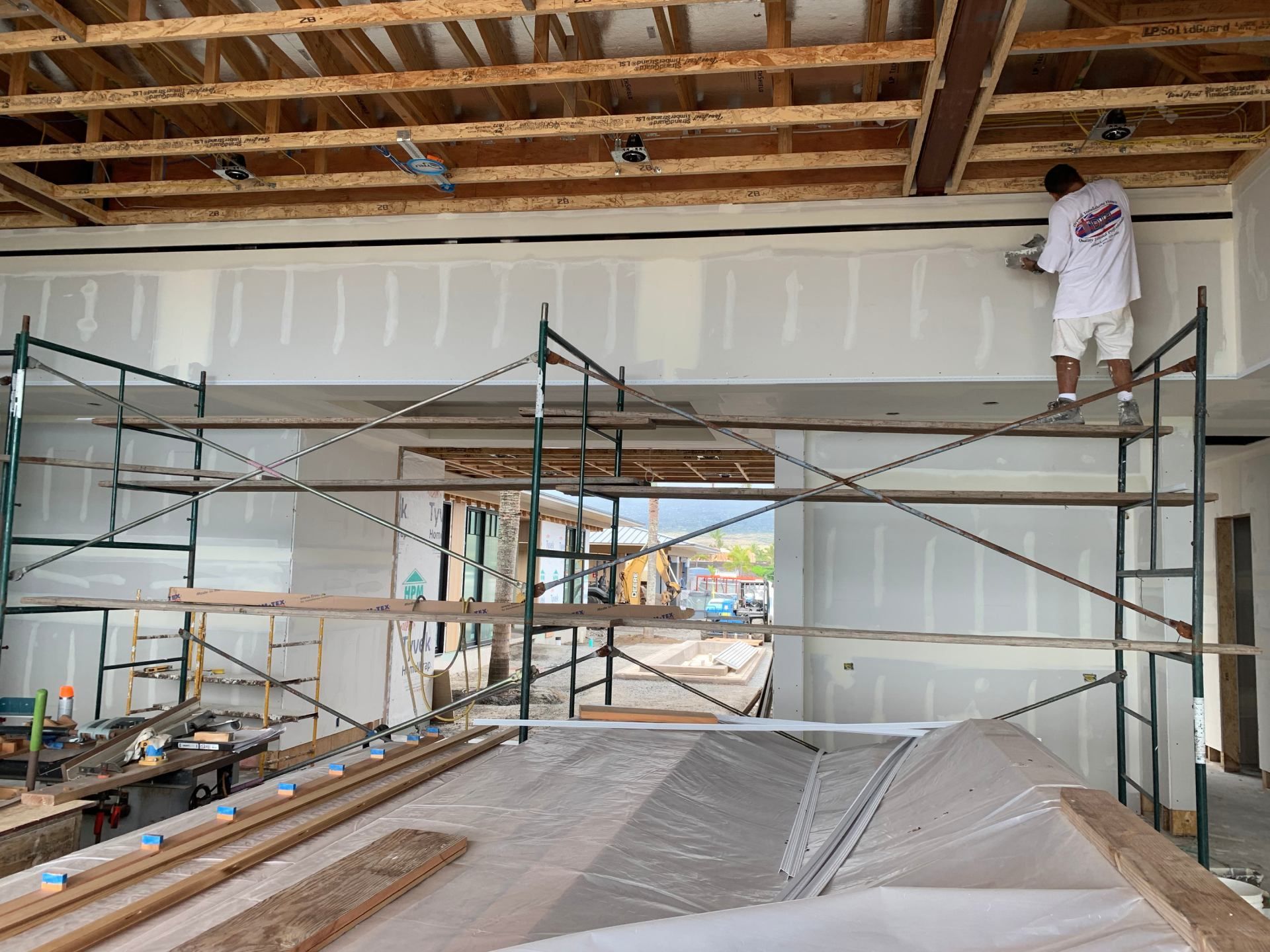 A man is standing on a scaffolding putting up drywall.
