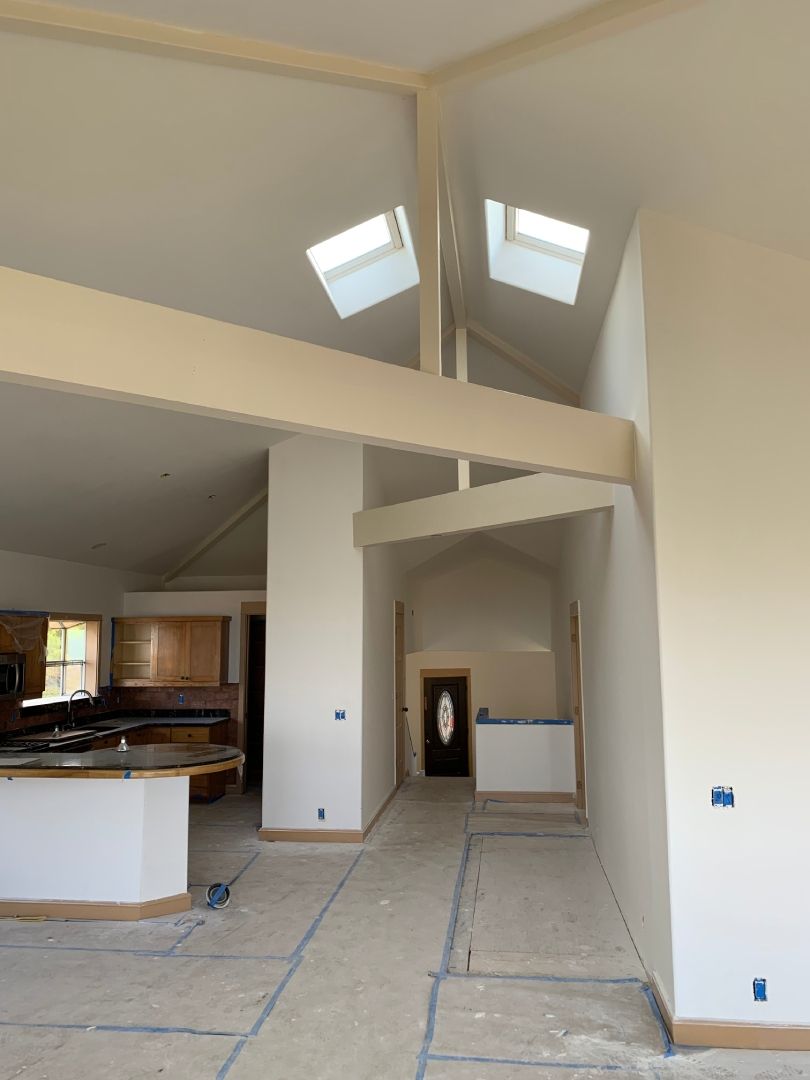 A large room with a vaulted ceiling and skylights with drywall.