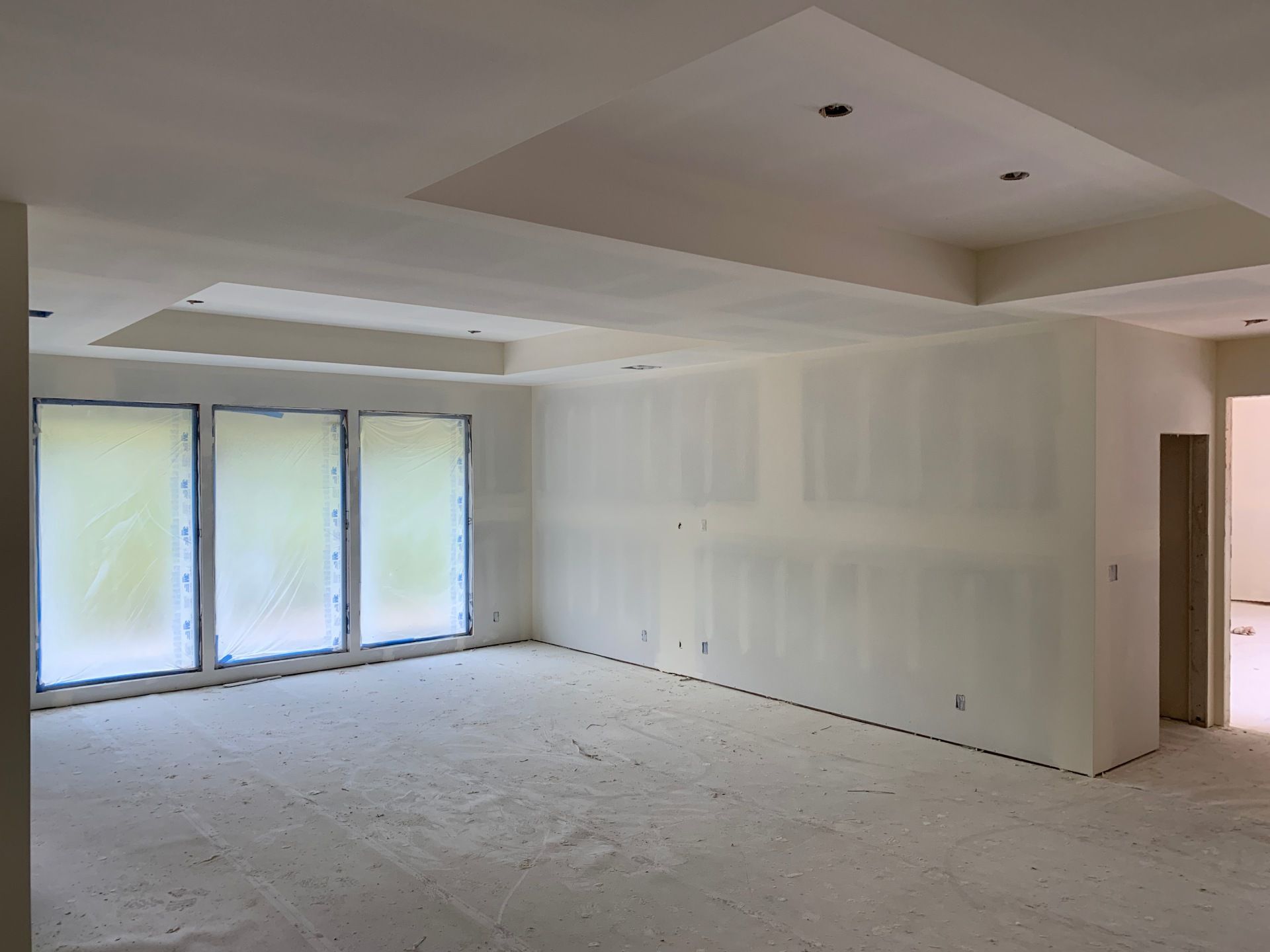An empty room with white walls and a ceiling with just installed and taped drywall.
