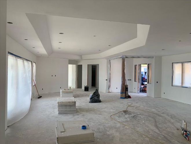 An empty room with white walls and a vacuum cleaner on the floor and just installed drywall.