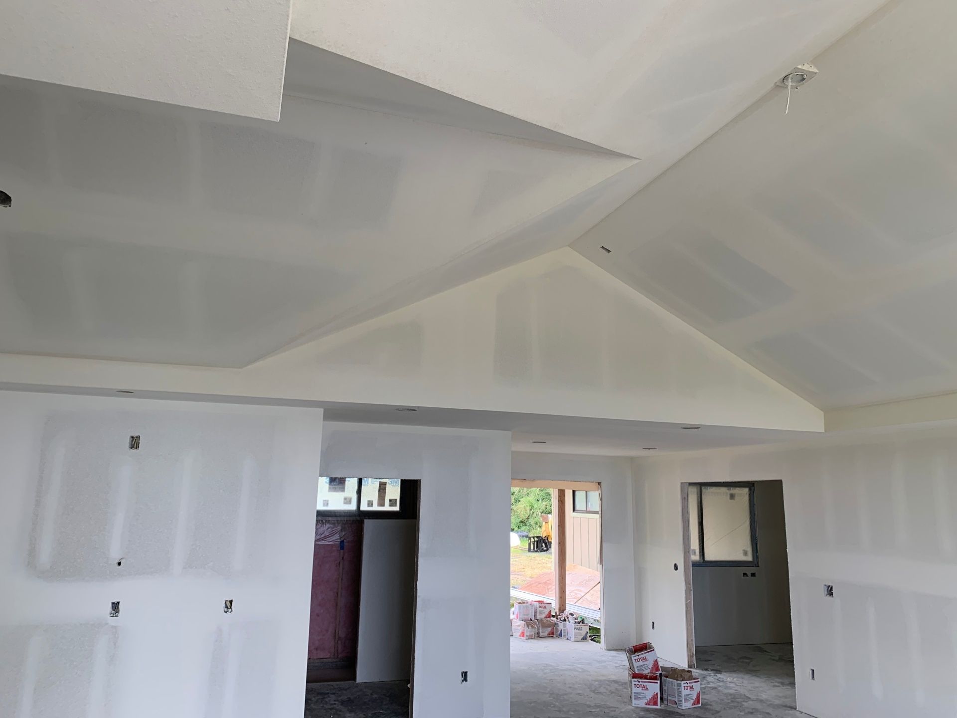 A room with white walls and a vaulted ceiling in a house under construction and just finished drywall installation.