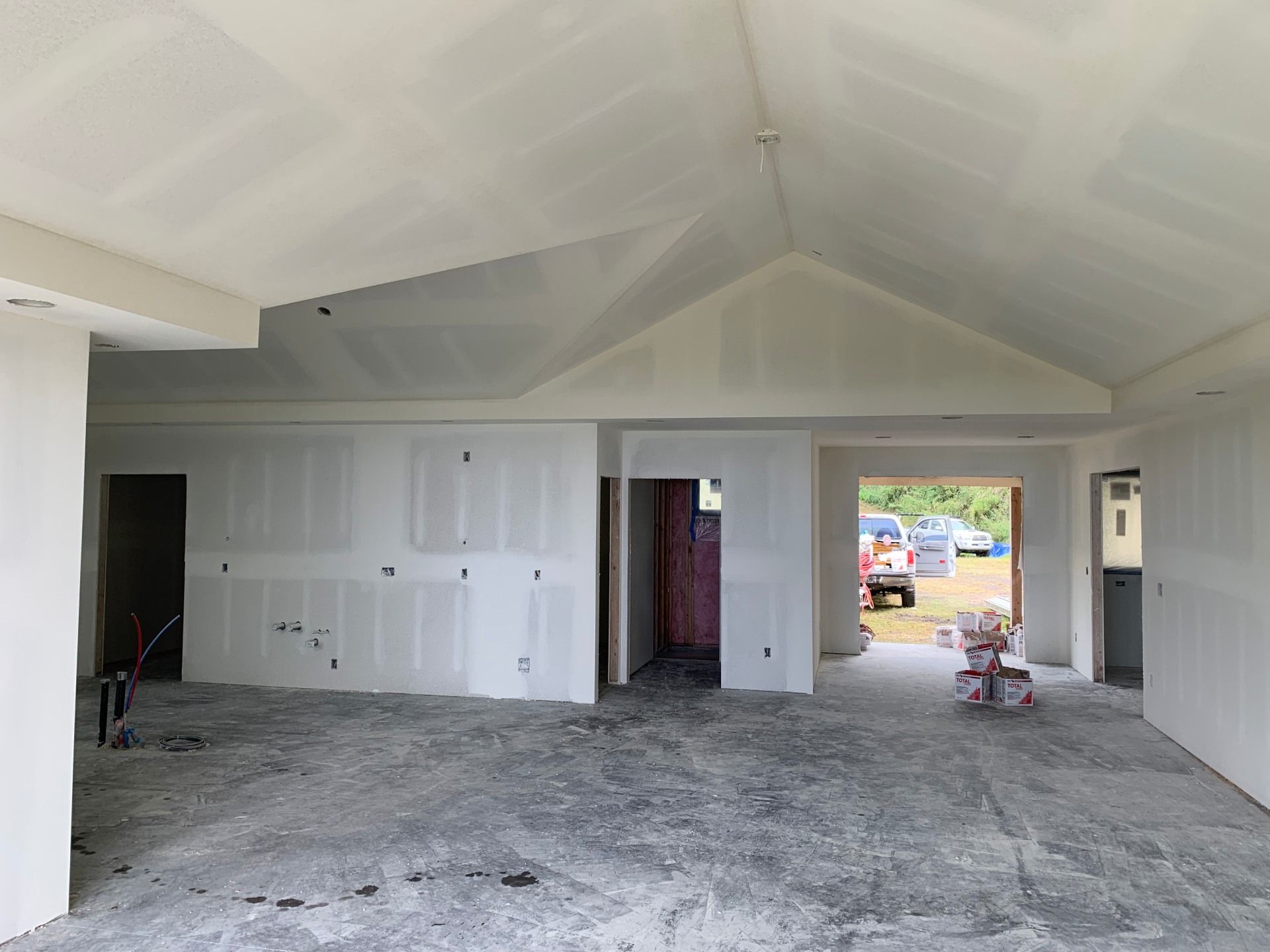 A large room with a vaulted ceiling is being built and drywall just installed.