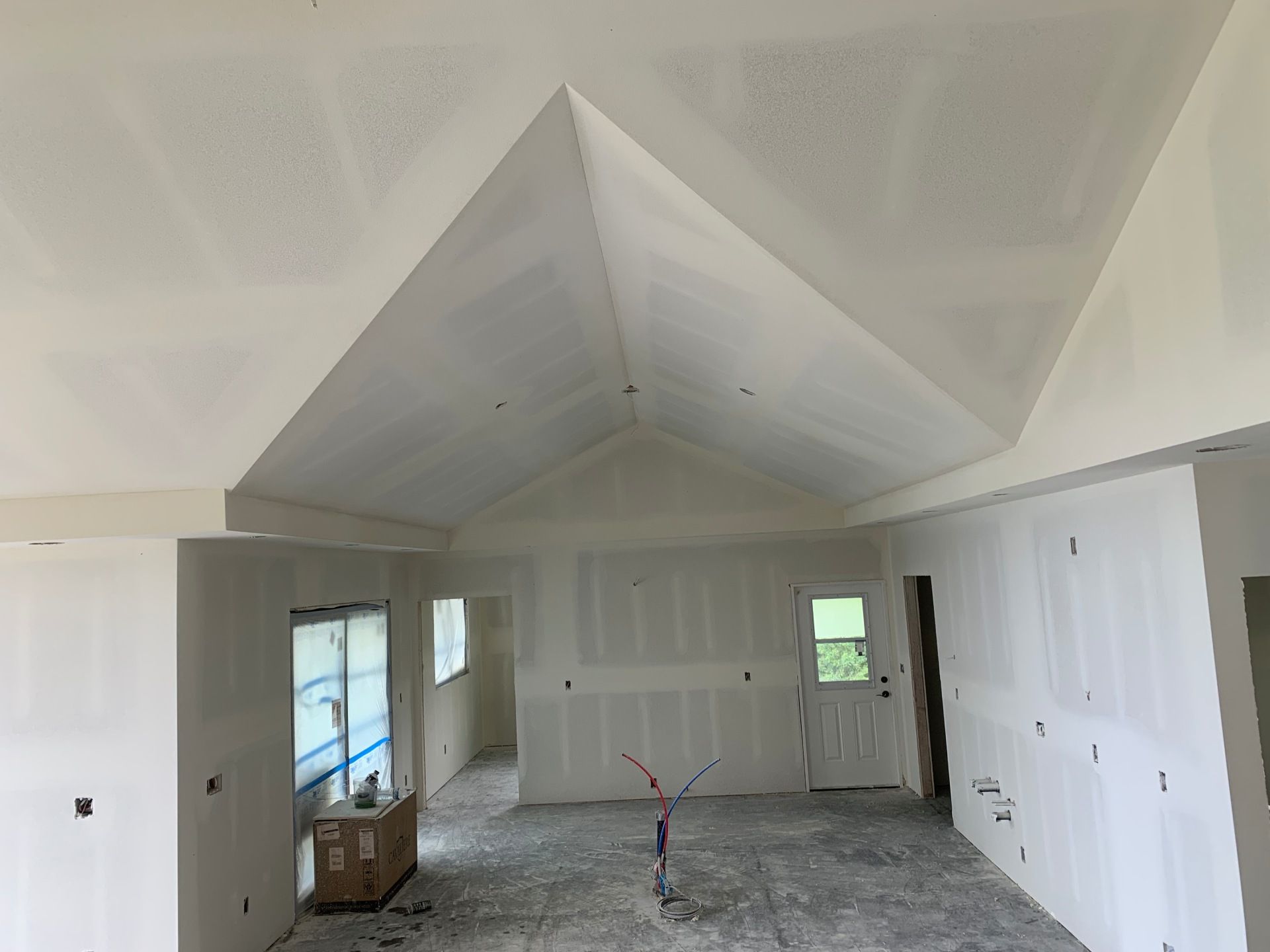 A large room with a vaulted ceiling in a house under construction and drywall installed.
