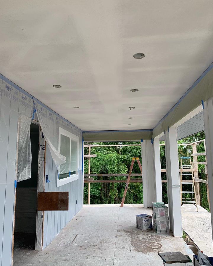 A large room with a ceiling that is being painted and roof has drywall. 