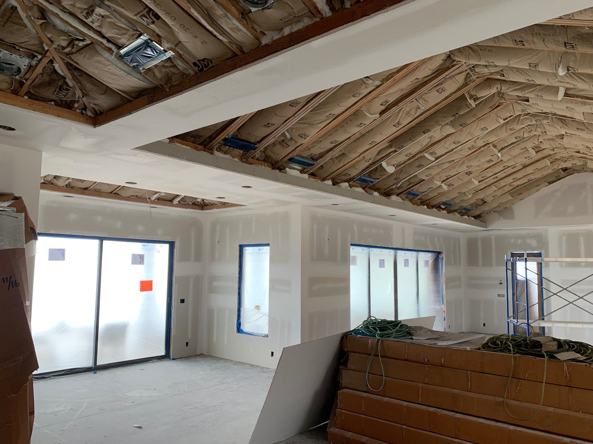 An empty room with a wooden ceiling and a lot of windows with completed drywall. 