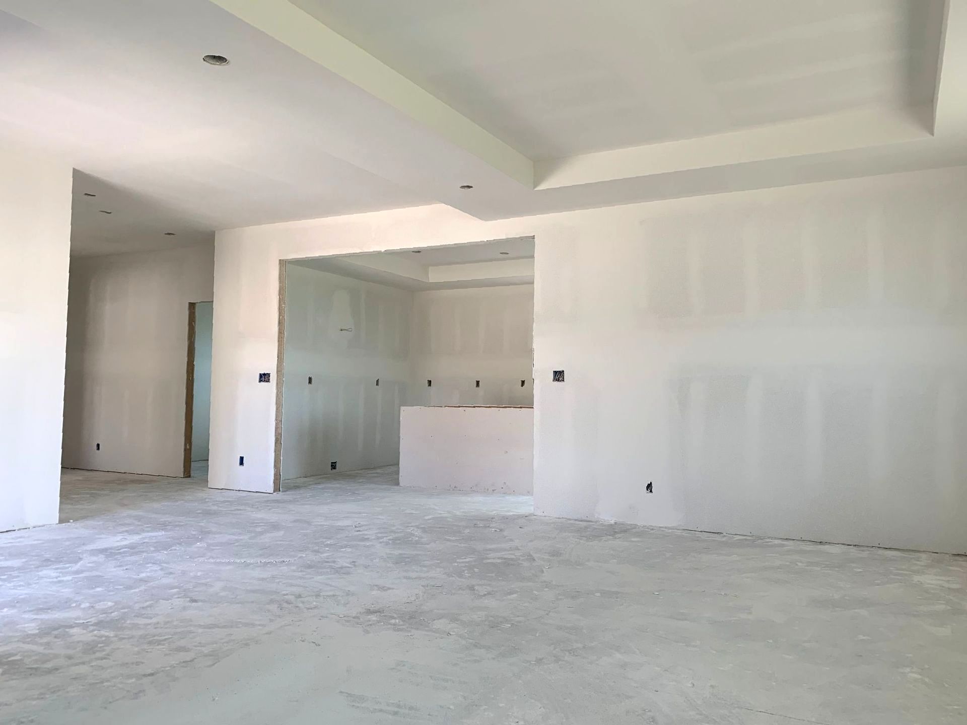 An empty room with drywalled walls and a concrete floor in a house under construction.