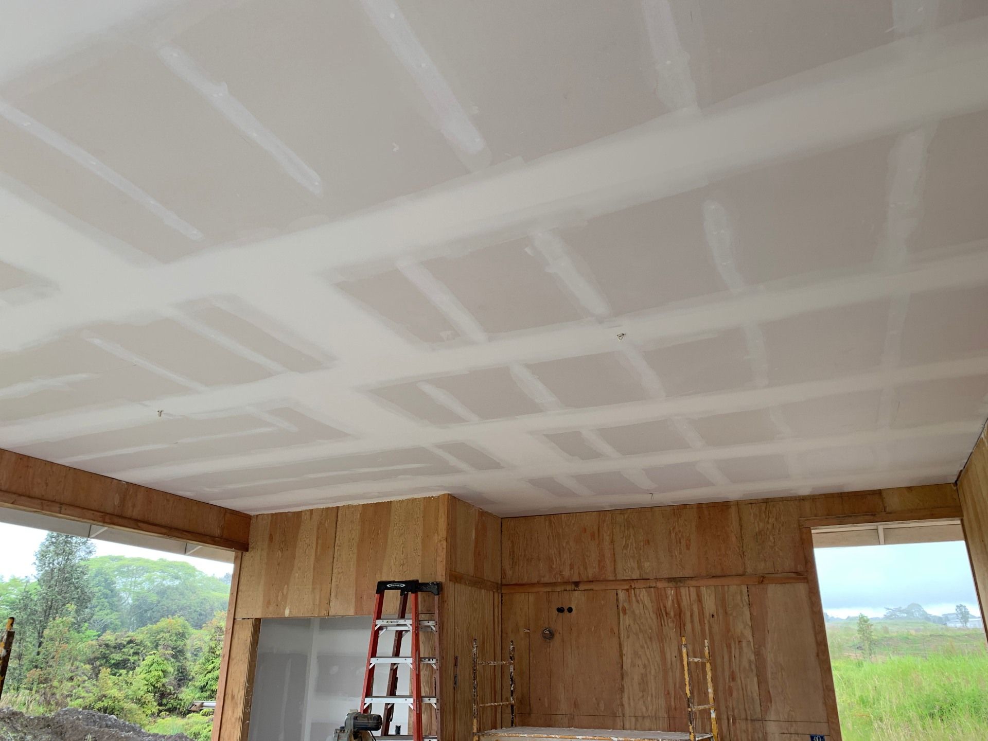 A room with a ladder in it and a drywall ceiling that is being built.