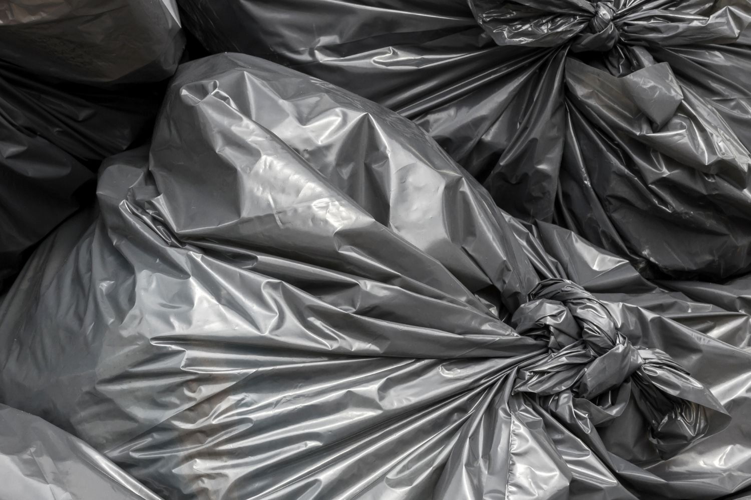 A pile of gray garbage bags are stacked on top of each other.