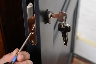 A person is fixing a door lock with a screwdriver.