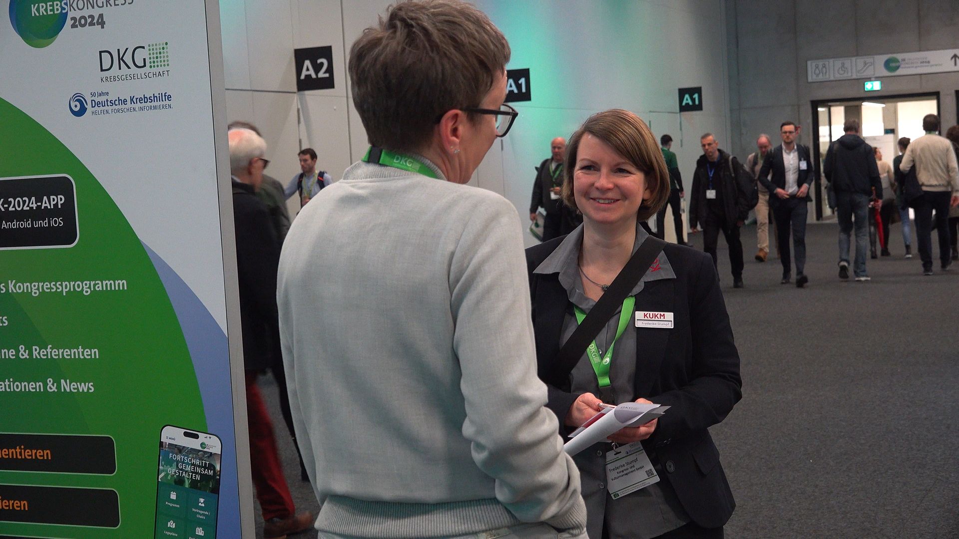 lachende KUKM Mitarbeiterin im Gespräch mit Teilnehmerin des deutschen Krebskongress 2024