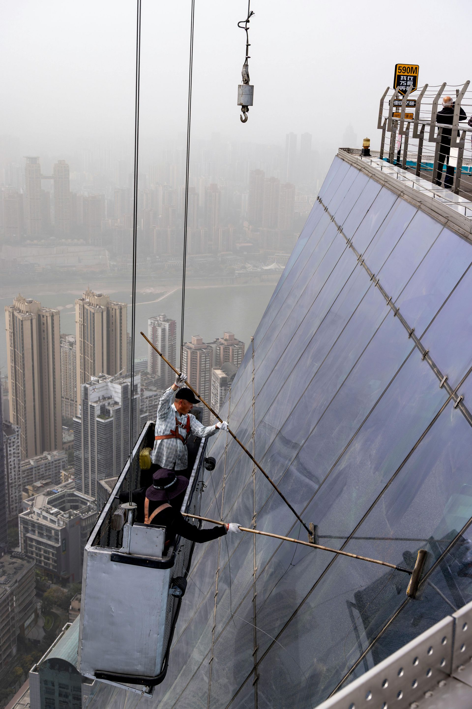 Window washers in a suspended platform clean a high-rise building with a city view.
