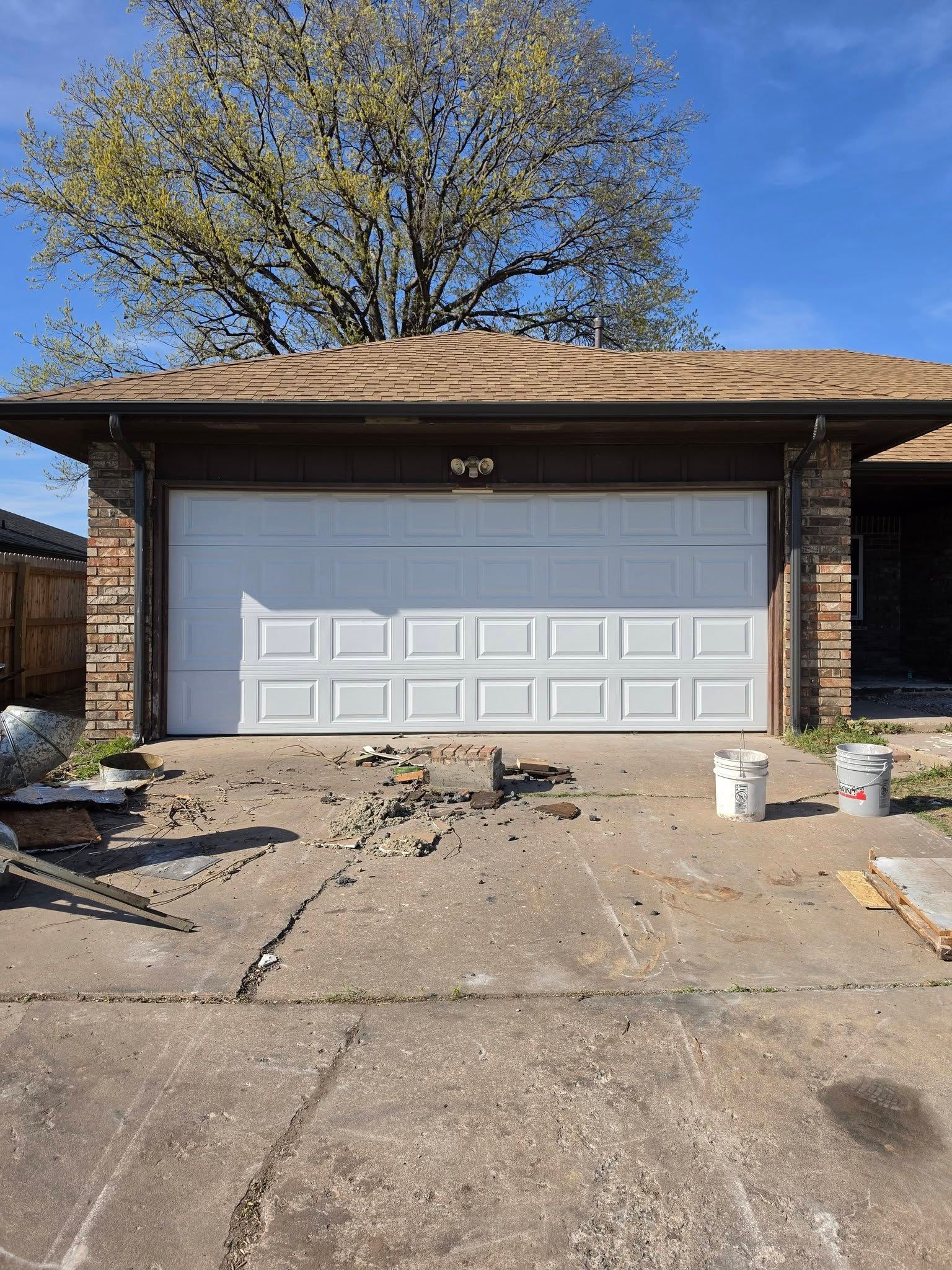 Brick house with a white garage door, concrete driveway, and construction debris in front.