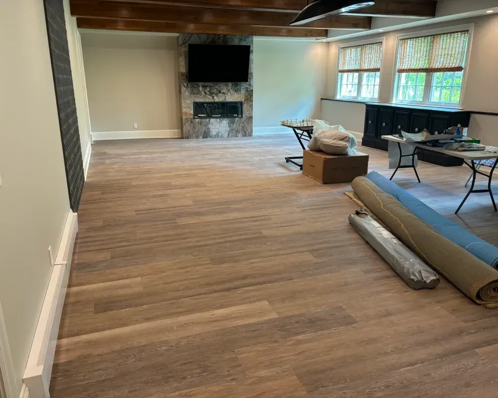 Newly installed wood-look flooring in a basement. Fireplace, bar and rolled rugs in room.