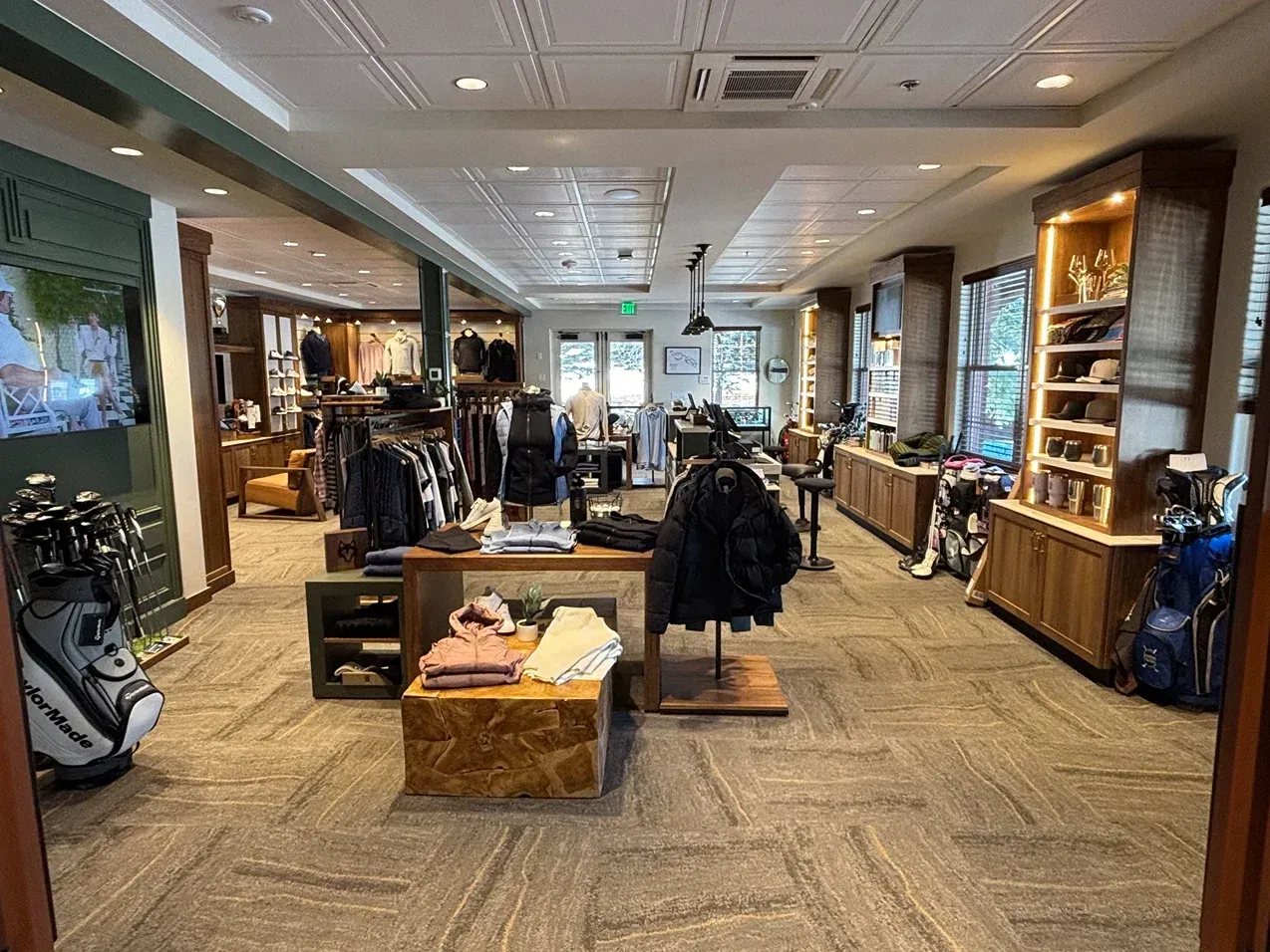 Golf shop interior with clothing displays, golf bags, and wooden shelves.