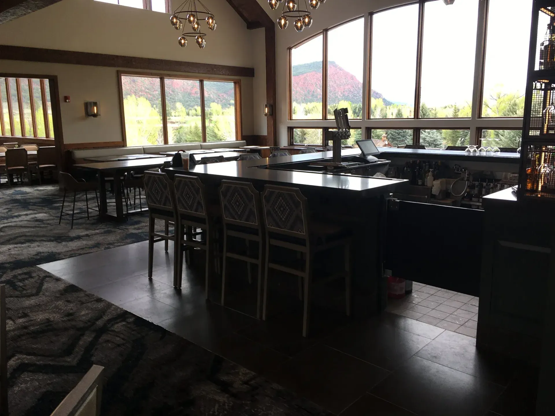 Bar with stools and tables, large windows overlooking a mountain and trees.