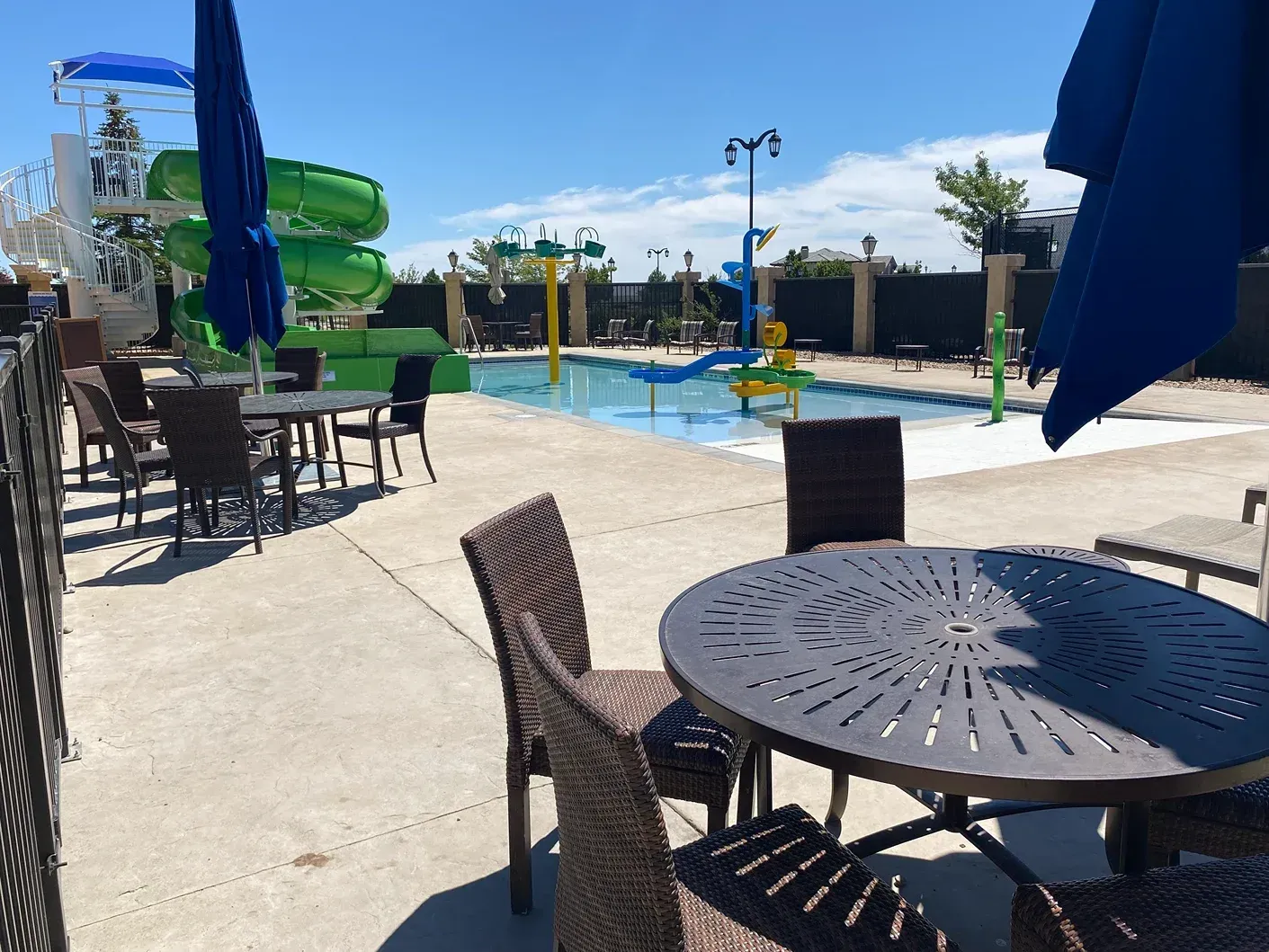 Outdoor pool area with tables, umbrellas, water slides, and clear blue sky.