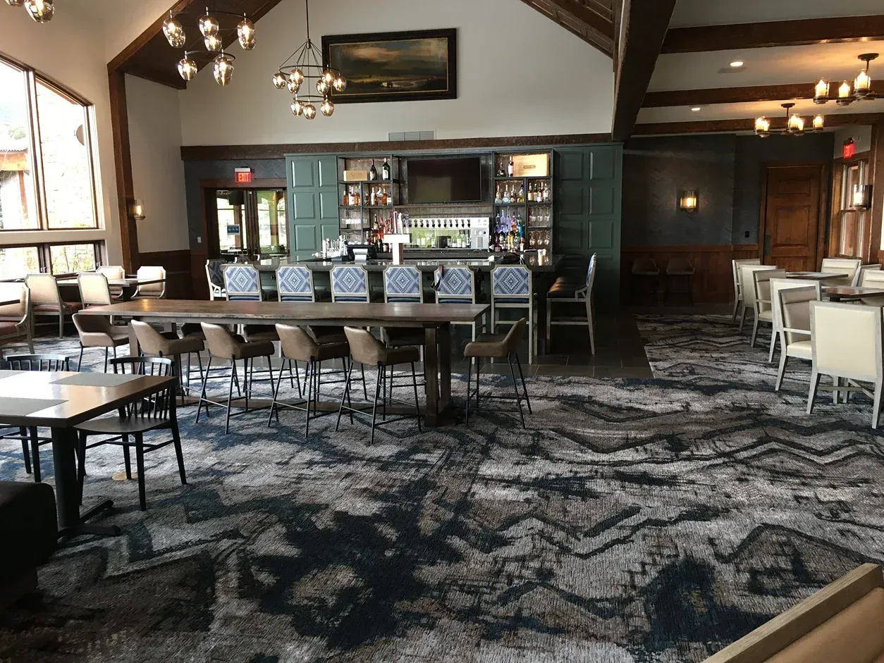 Interior of a bar/restaurant with seating, long tables, and a bar. Carpet has a blue and grey pattern.