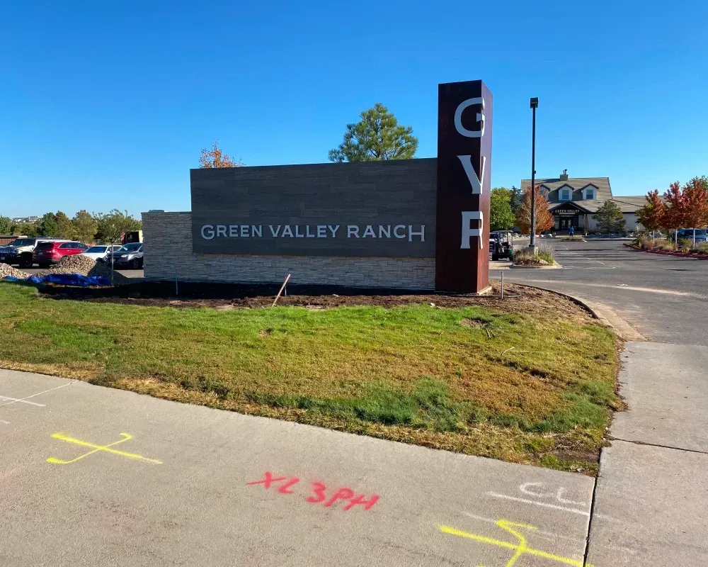 Sign for Green Valley Ranch in a grassy area with a blue sky. The letters GVR are visible.