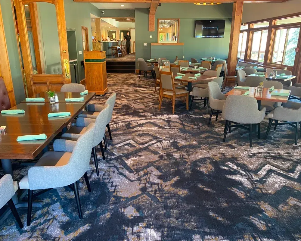 Restaurant dining room with tables, chairs, and patterned carpet. Green walls and wooden accents.