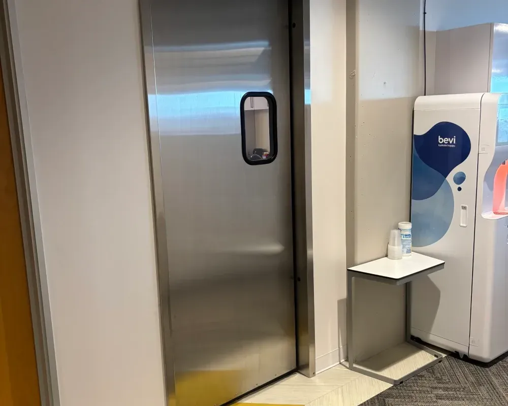Stainless steel door with a small window, next to a water dispenser and small shelf.