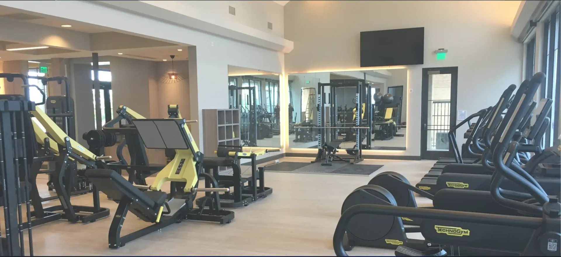 Gym interior with exercise machines, mirrors, and a TV on the wall.