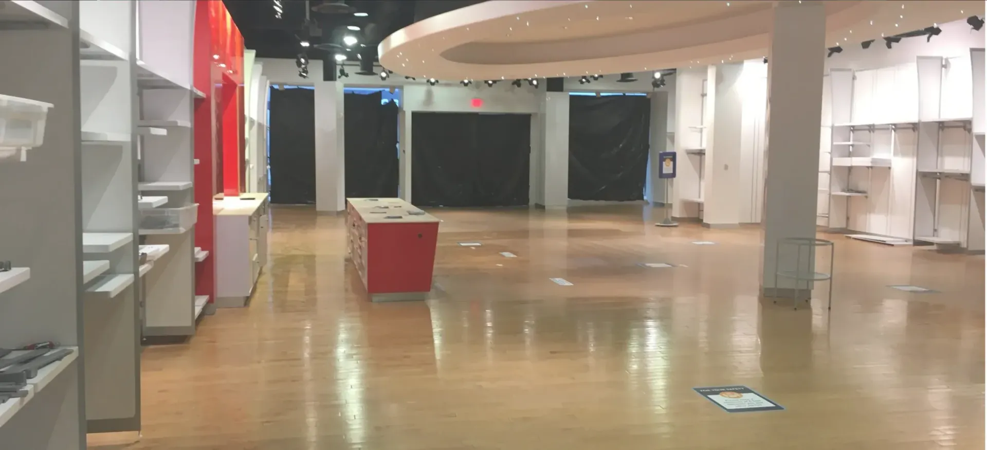 Empty store interior with wooden floors, white walls, and a red display.