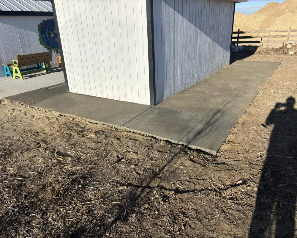 Concrete ramp next to white building, leading to a dirt and gravel yard.