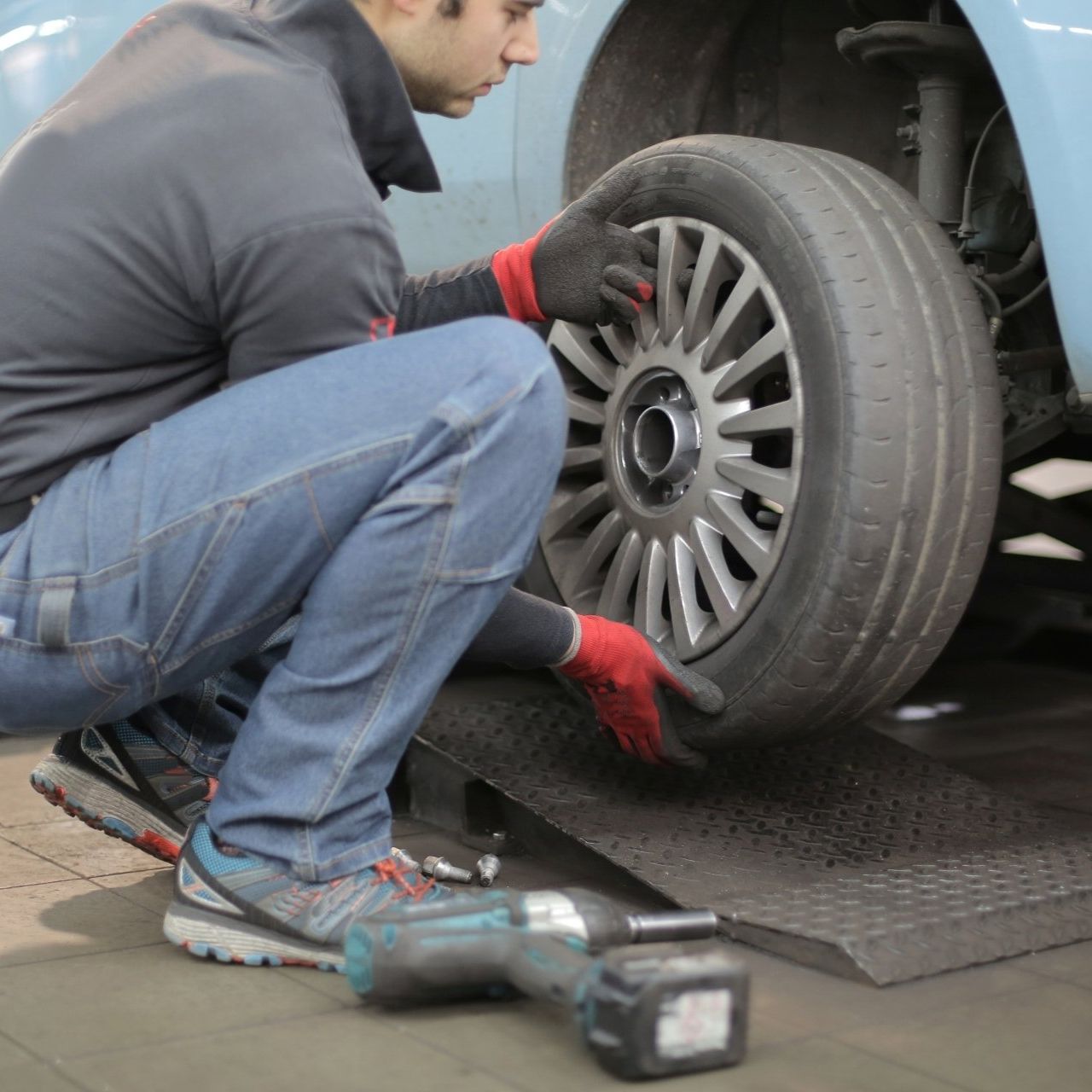A man is kneeling down to change a tire on a car