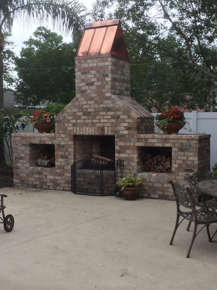 A brick fireplace with a copper roof is sitting on a patio next to a table and chairs.